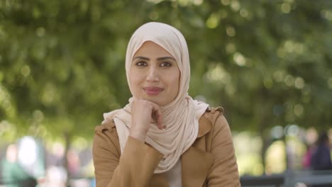 Retrato-De-Una-Mujer-Muselina-Sonriente-Con-Hijab-Sentada-En-Una-Mesa-Al-Aire-Libre-En-Las-Calles-De-La-Ciudad